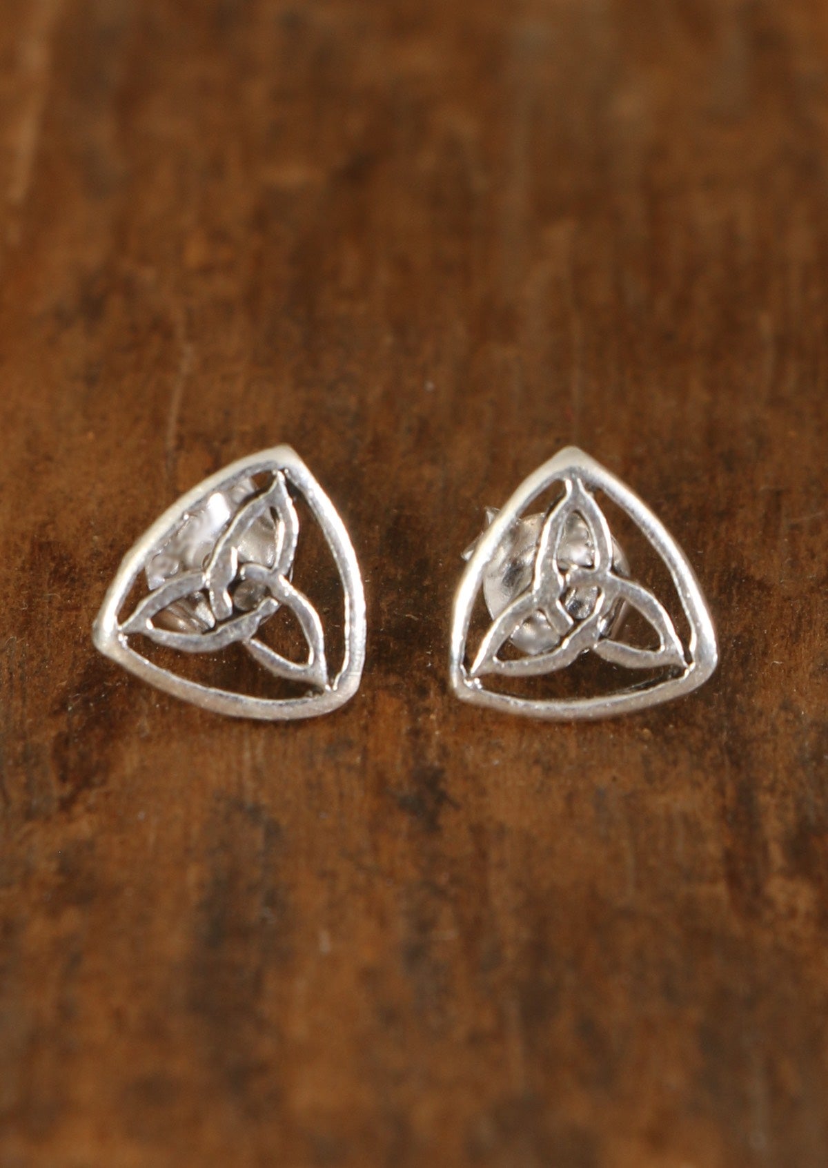 A pair of sterling silver Celtic Triangle stud earrings featuring a Celtic triangle design, displayed against a wooden background.