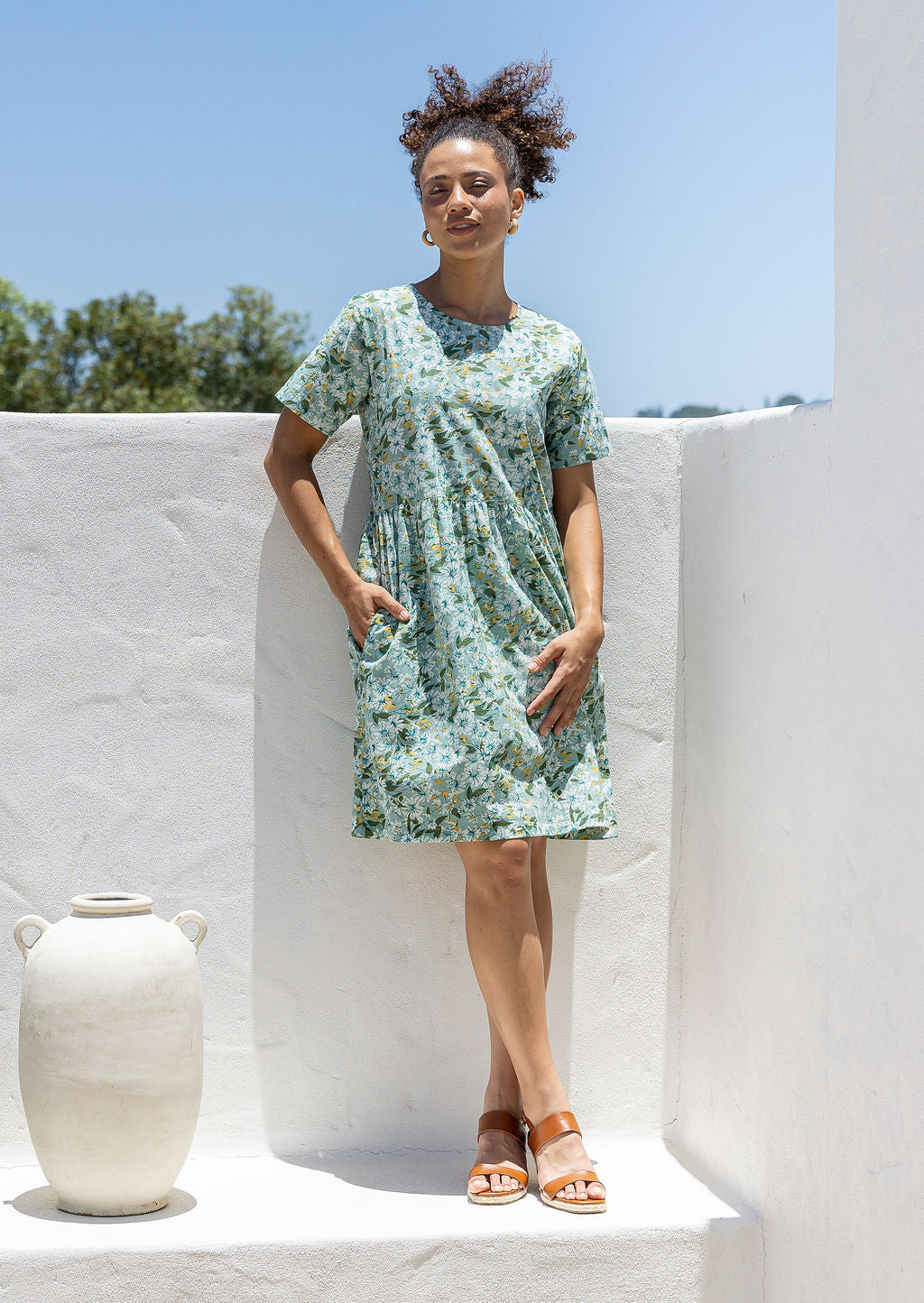 Woman wearing a above knee length floral cotton dress with short sleeves, pockets and round neckline