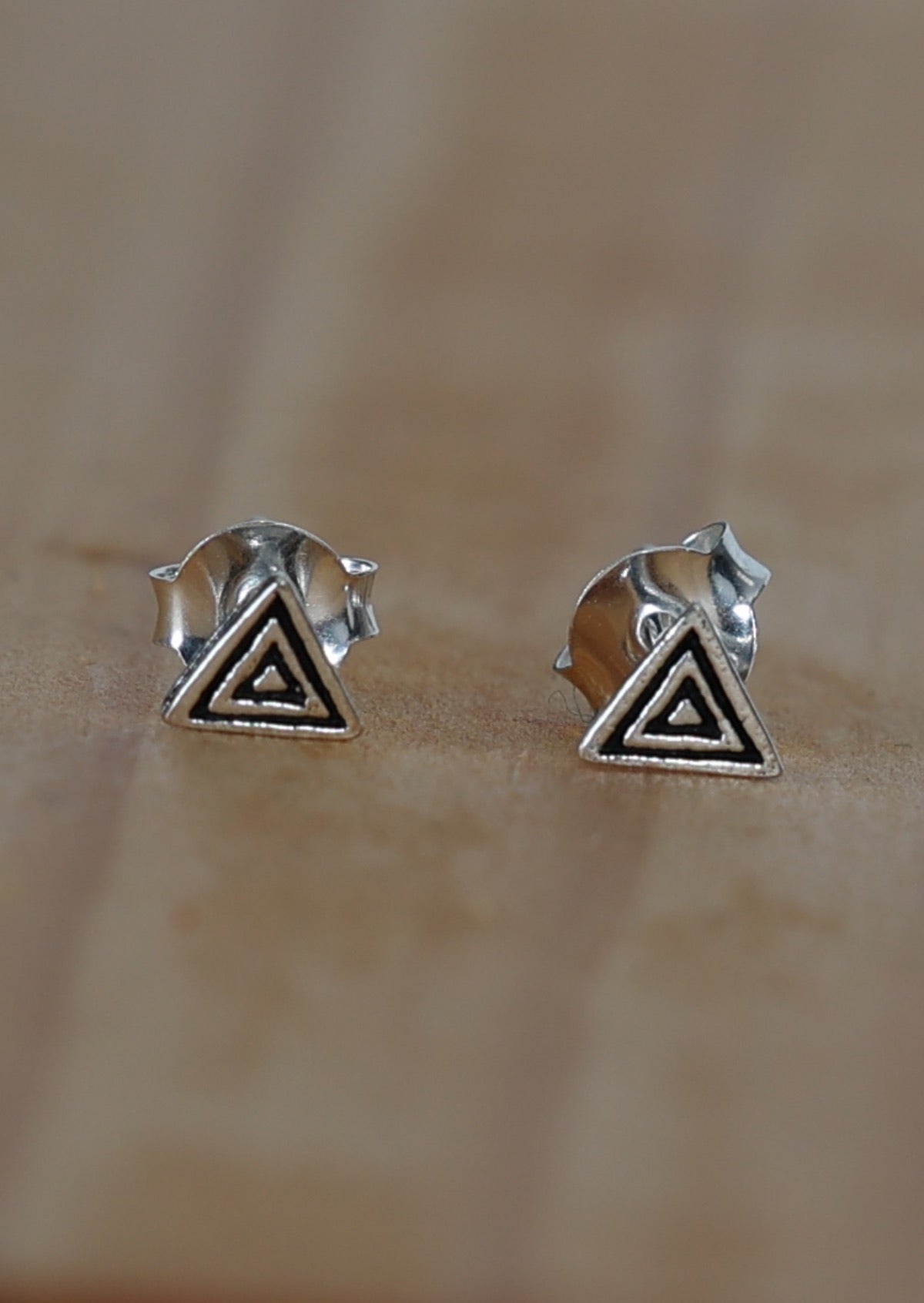 A pair of sterling silver triangular studs with a rippled texture design, displayed against a wooden background