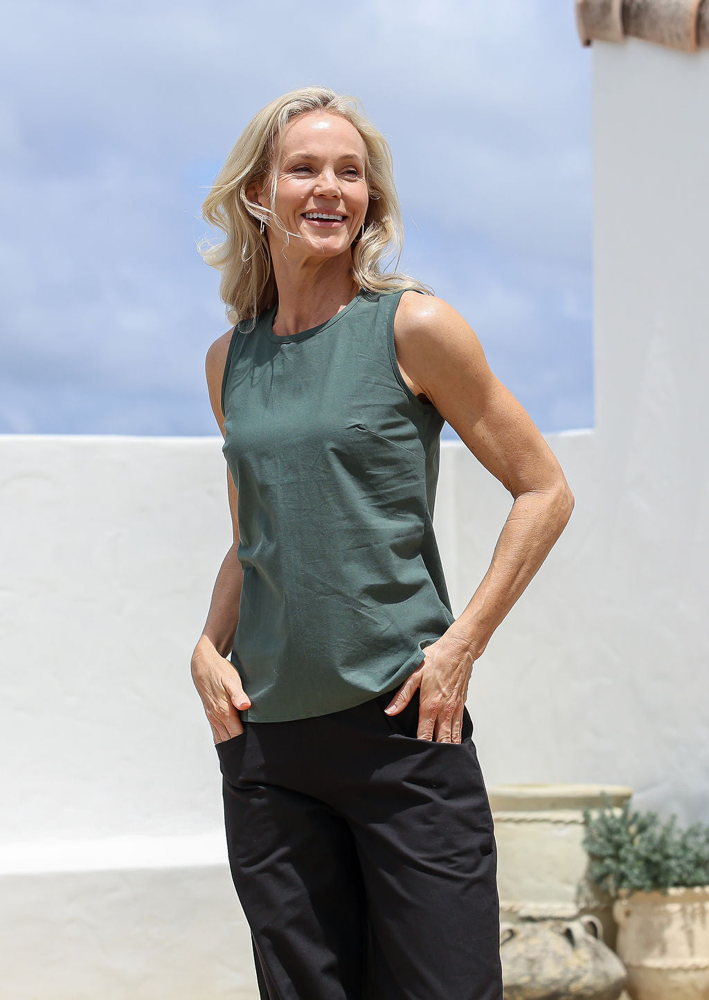 Woman wearing a relaxed fit 100% cotton green sleeveless top and black pants standing outdoors