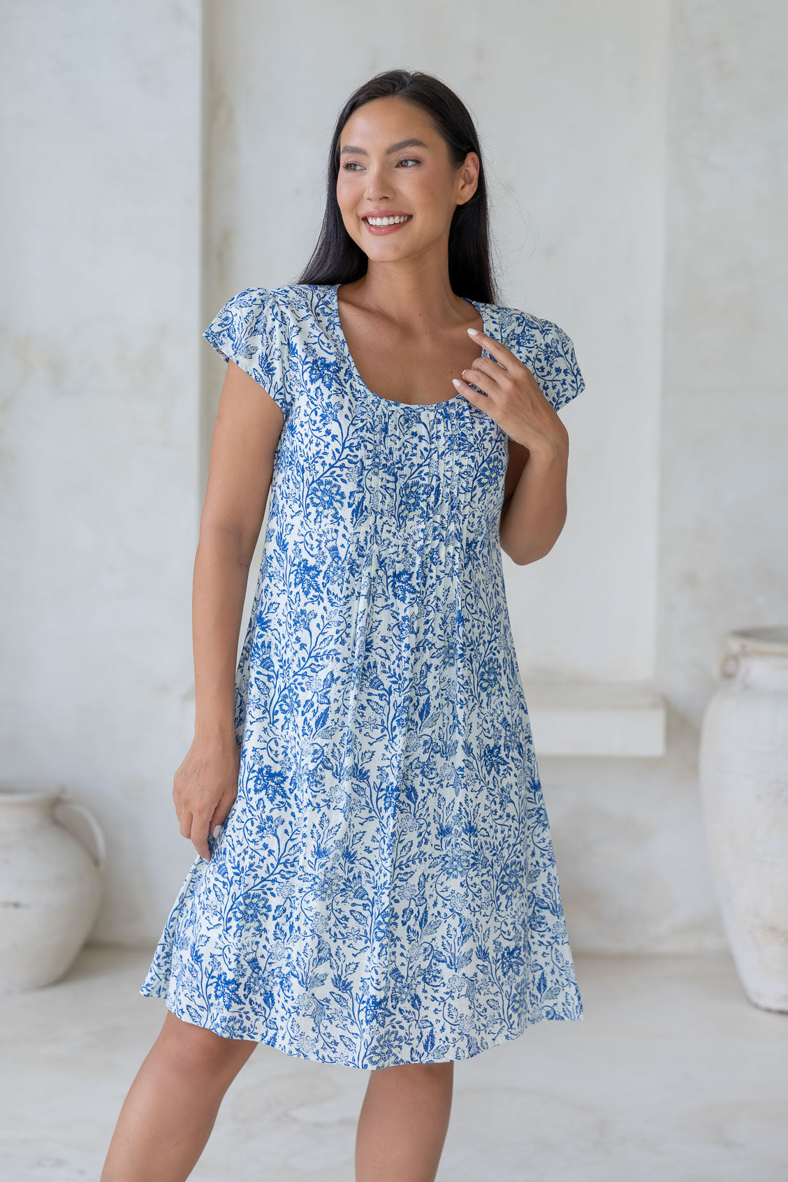 Woman wearing a cap sleeved 100% cotton dress with fitted bodice and a-line skirt in white based blue floral print.