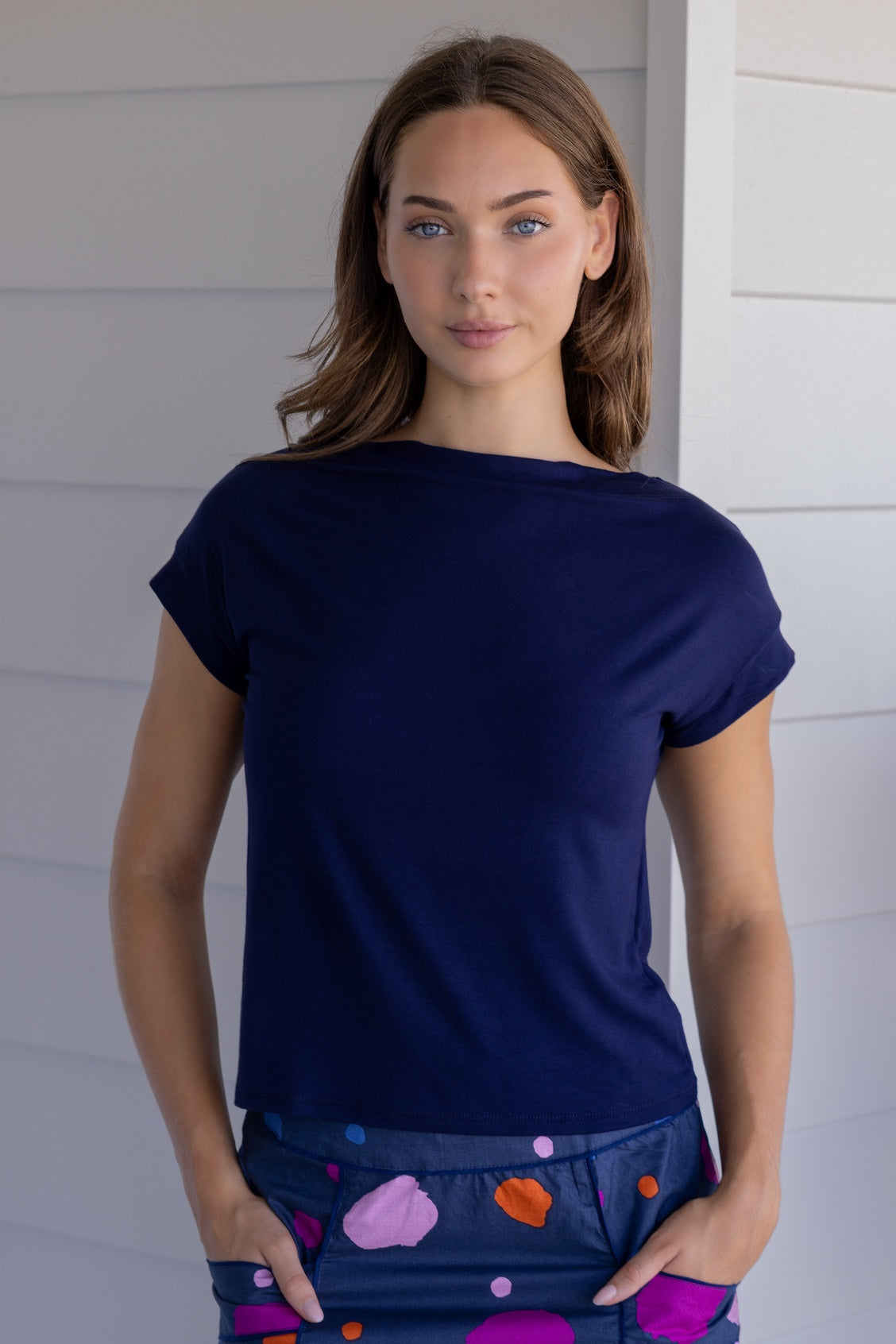 Woman wearing a navy blue soft stretch rayon jersey top with a high wide neckline and short sleeves, with hands in skirt pockets