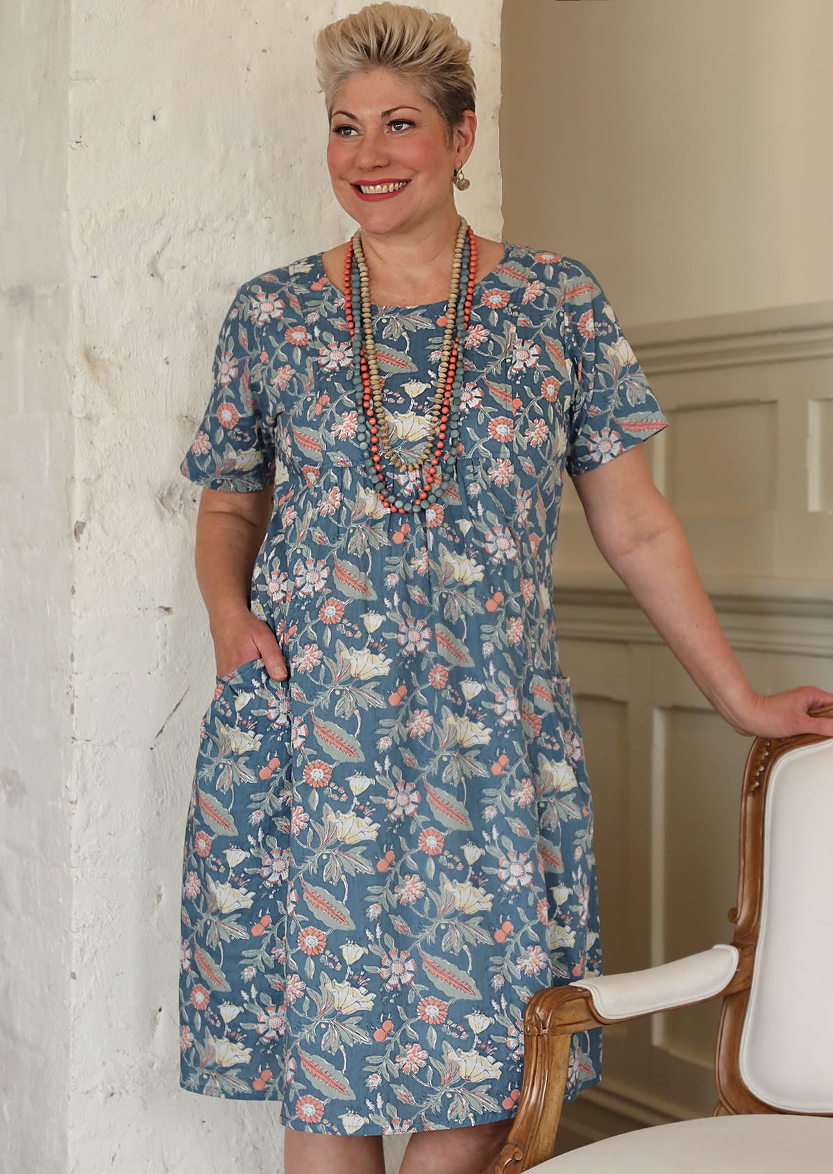 Woman wears floral print over the knee length cotton dress paired with wooden beaded necklaces