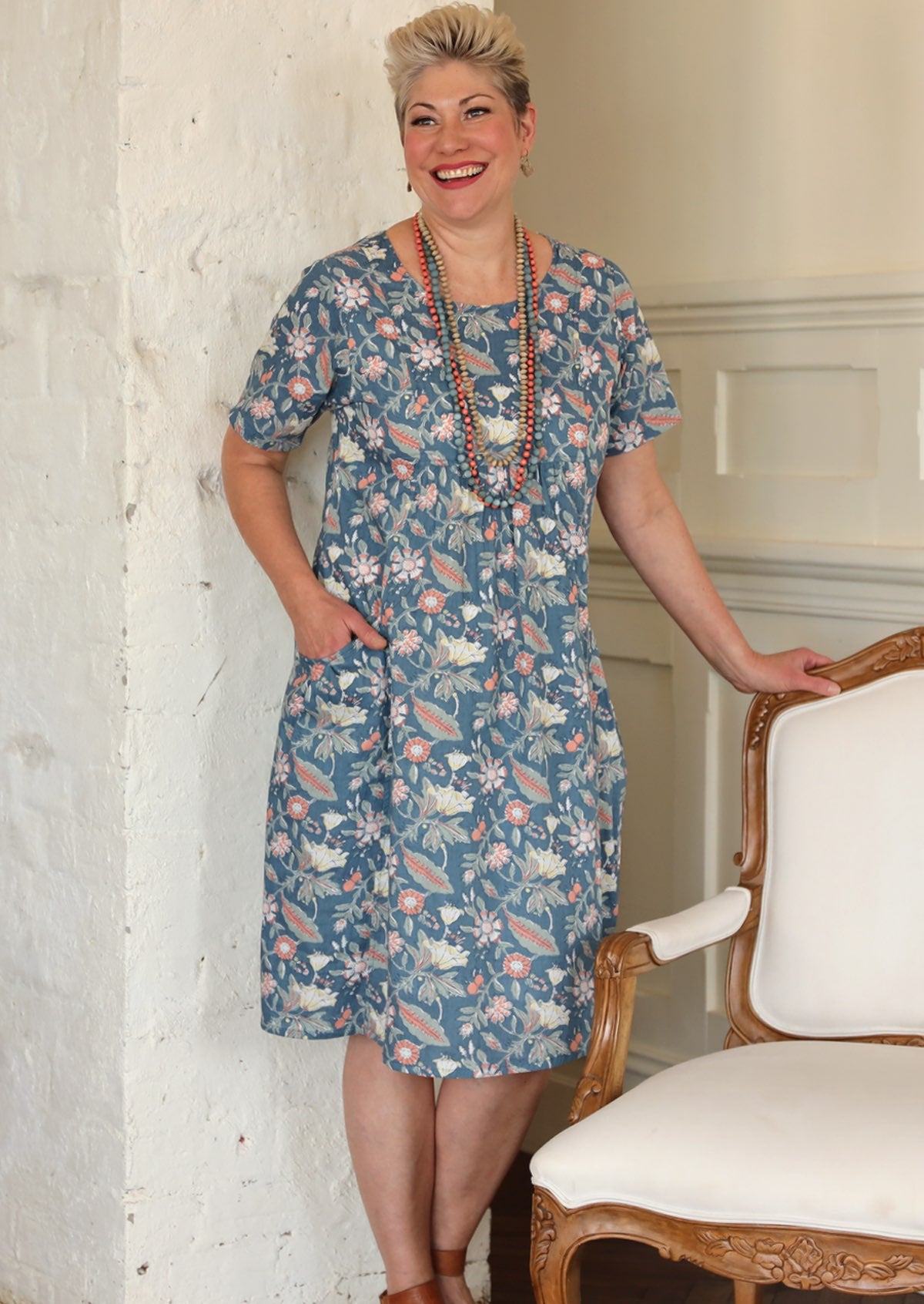 Woman stands in cotton floral relaxed fit dress with short sleeves and round neckline, with a hand in pocket