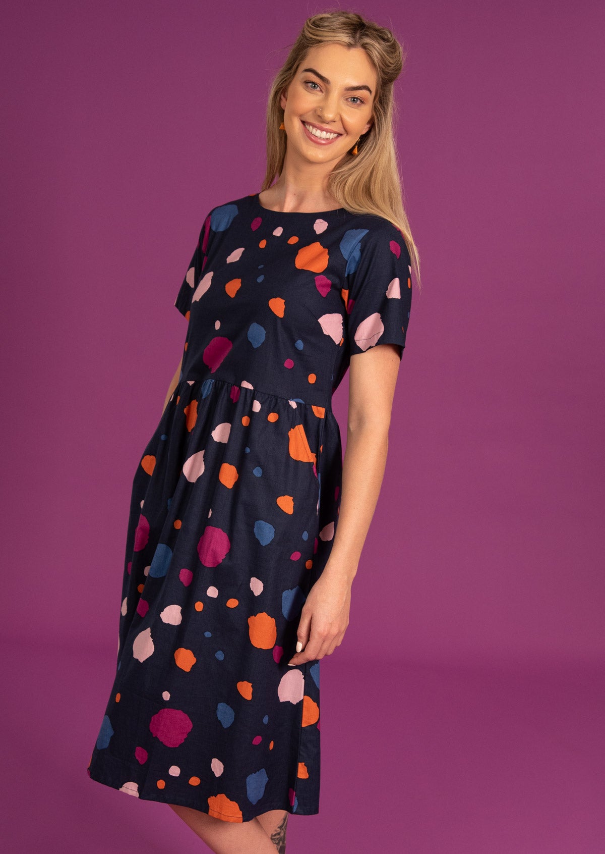 Model posing in loose fit short sleeve dress with pockets and high round neckine.
