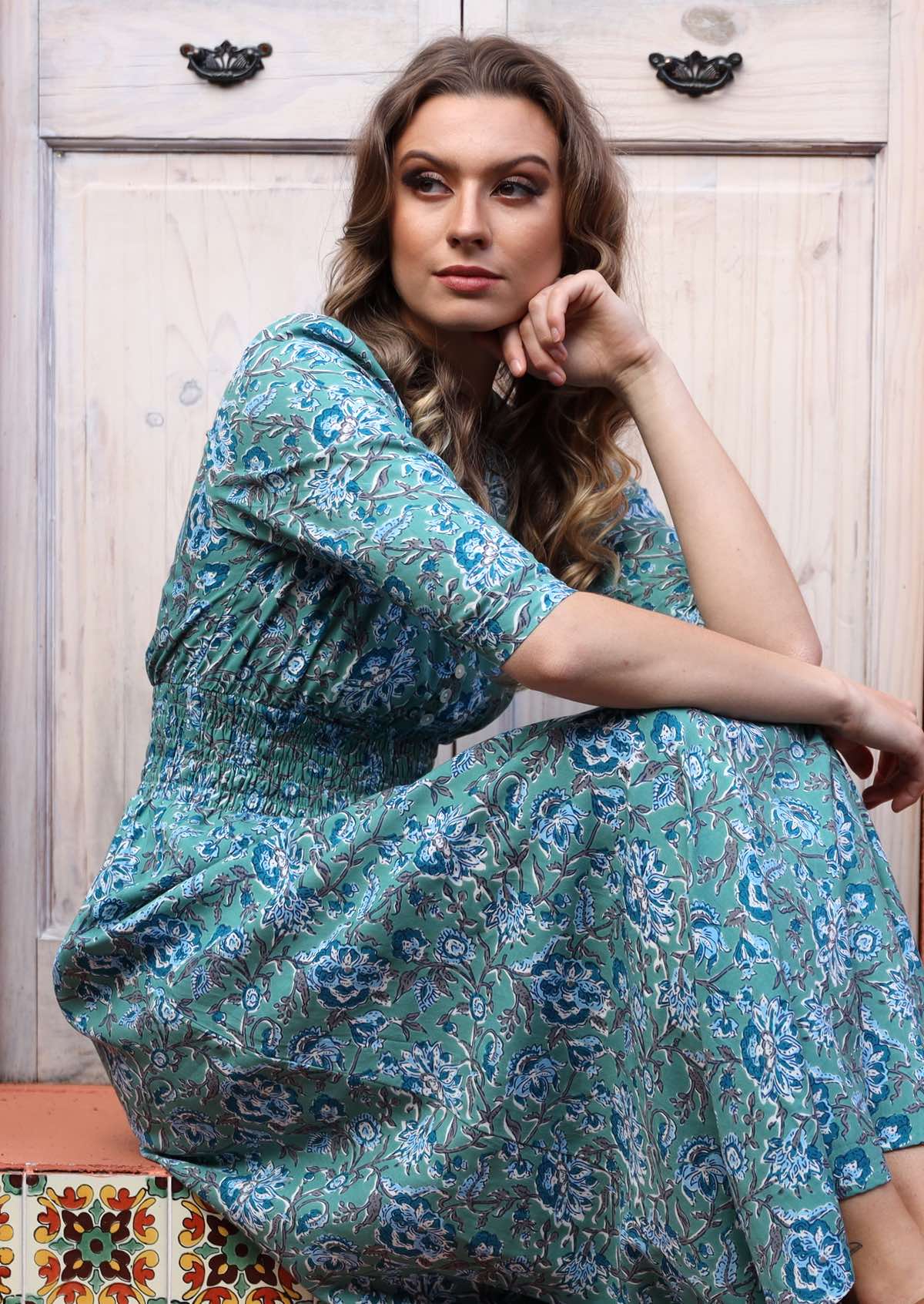 Woman sitting in aqua blue based long rayon dress with 3/4 sleeves and ruched waistband.
