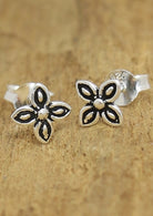 A pair of Zieria silver stud earrings with a floral design, displayed against a wooden background
