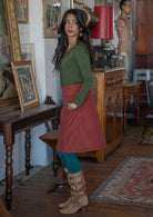 Woman poses side to the camera in an A-line knee length burnt henna skirt, paired with an olive top and teal leggings