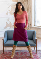 Model poses in corduroy A-line knee length skirt in plum purple, with her hands in the pockets