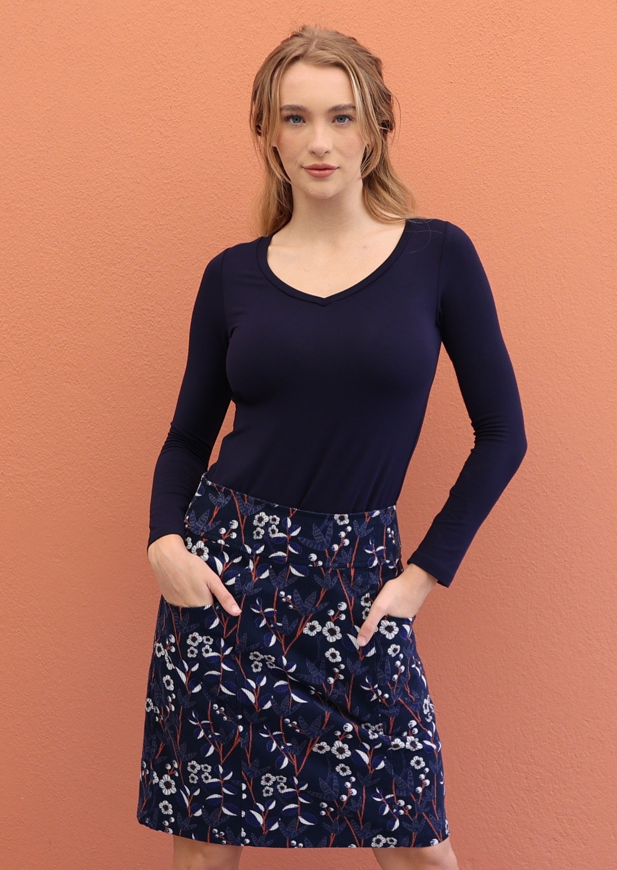 Model wears gorgeous floral print on navy blue based cotton corduroy skirt with both  hands in pockets.