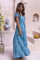 Woman in a aqua floral maxi dress standing in an indoor setting with decorative elements.