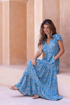 Woman in a blue floral dress sitting on steps with classical architecture in the background