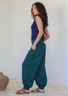 Woman poses with hands in pocket wearing a lightweight deep teal cotton pants with cuffed ankles and elastic at back waist