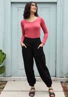 Model posing in black 100% cotton harem pants paired with a pink top and with hands in pockets