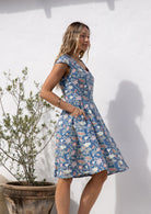Model stands side ways in retro style 100% cotton blue floral with cross over bodice and pockets, fit and flare style 