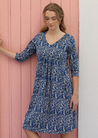 Woman wears cotton over the knee length dress with 3/4 sleeves, V-neckline and empire waistline