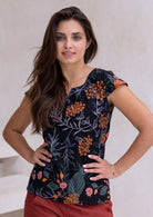Woman poses in cap sleeved cotton tailored top in black based botanical print with orange and pink florals.