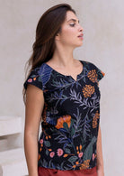 Woman wearing cap sleeved black based botanical print top with orange, pink florals and blue, grey and green leafy print.
