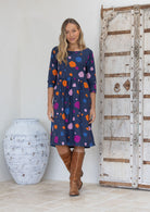 Woman wearing a blue based dress with colourful polka dots standing next to a wooden door.