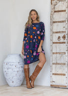 Woman wearing a cotton knee length dress with orange, blue, plum and pale pink spots on a navy blue base, paired with tan boots