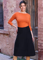 Woman wearing a-line below knee length black corduroy skirt with bright orange top 