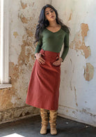 Woman with dark hair wears an olive long sleeve rayon top with a midi length corduroy skirt in burnt henna