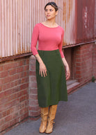 Woman wears green corduroy A-line midi length skirt with belt loop, paired with a 3/4 sleeve rayon top in pink