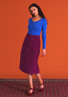 woman wearing purple corduroy aline skirt  with belt loops with bright blue v-neck long sleeve top 