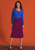 woman wearing purple corduroy aline skirt  with belt loops with bright blue long sleeve top with burgundy shoes