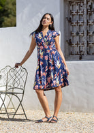 Woman wearing a retro style 100% cotton, floral dress standing outdoors against a white wall.
