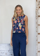 Woman wearing a navy sleeveless cotton top with floral pattern that sits above the hips, paired with navy pants
