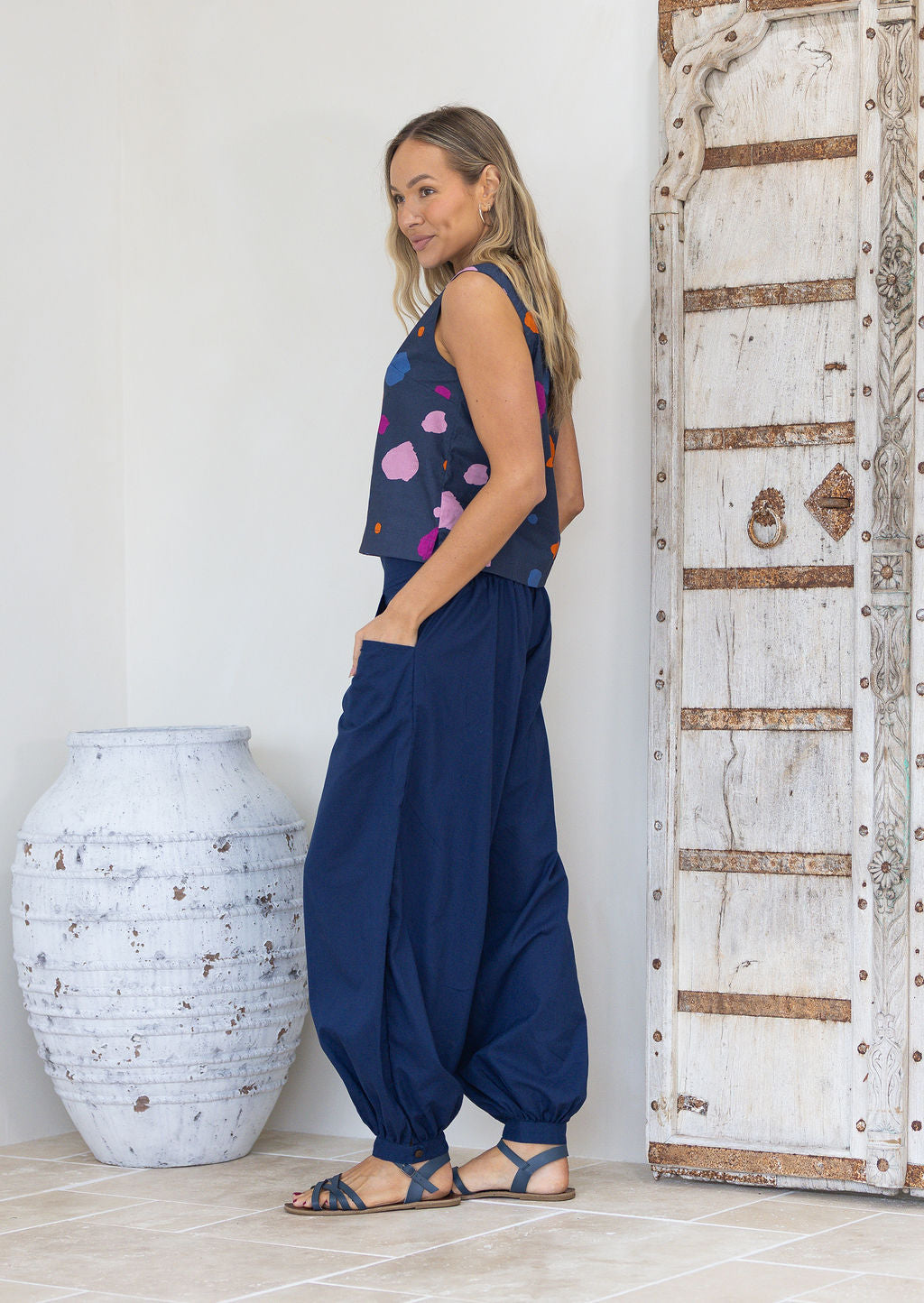 Woman wearing a navy based cotton sleeveless top standing next to a textured white vase and wooden door.