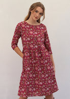 Model is wearing 100% cotton dress in sweet red cranberry base with pink florals, 3/4 sleeves and pockets.