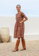 Model wearing relaxed fit, knee length cotton dress with wide round neckline and hands in pocket.