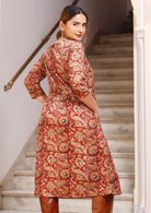 Back image of model with hands in pockets of red based floral print dress featuring button closure back