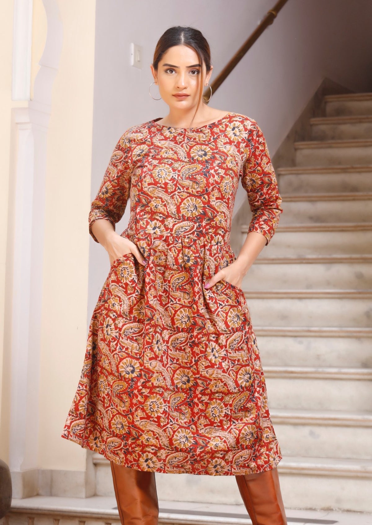 Model in knee length cotton dress with 3/4 sleeves, wide round neckline and hands in pocket.