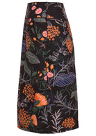 Side view of knee-length cotton pencil skirt with side zipper and piped details in retro floral print with orange, pink, blue, and green on black base