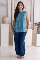 Woman wearing a blue 100% cotton patterned top and dark blue cotton pants in a decorative setting.