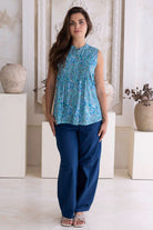 Woman wearing a blue cotton floral top and navy pants standing in a room with decorative elements.