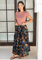 Woman wearing a midi length button through cotton floral skirt paired with a dusty pink fitted top