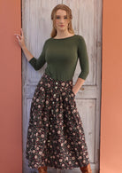 Woman standing in front of white door with one hand on door frame wears black based white and maroon floral print cotton button through skirt other hand in pocket