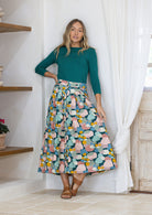 Woman wearing a teal top and pastel print shin length skirt with box pleats and belt loops