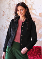 Woman wearing black corduroy jacket with brass buttons and pockets over green corduroy pants 