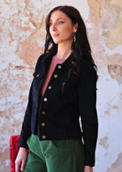 Woman wearing black cotton corduroy jacket with brass buttons and pockets over green corduroy pants 