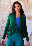 Model wears forest green long sleeve stretch rayon cardi with a waterfall front hem that is cropped at the front, exposing electric blue top underneath