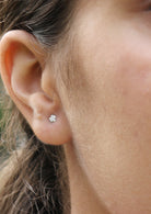 Close-up of an ear wearing a small dainty flower silver studs with soft petals arranged in a bloom