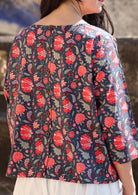 Back of woman in a cotton relaxed fit 3/4 sleeve top with decorative buttons, in a red and green floral print on a blue base 