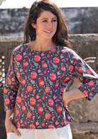 Woman in a cotton relaxed fit 3/4 sleeve top in a red and green floral print on a blue base 