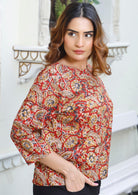 Model wears loose fit cotton top in warm toned floral pattern on red base.