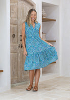 Woman holding skirt out to the side of a blue floral sleeveless, knee length dress with a V-neckline and buttoned bodice